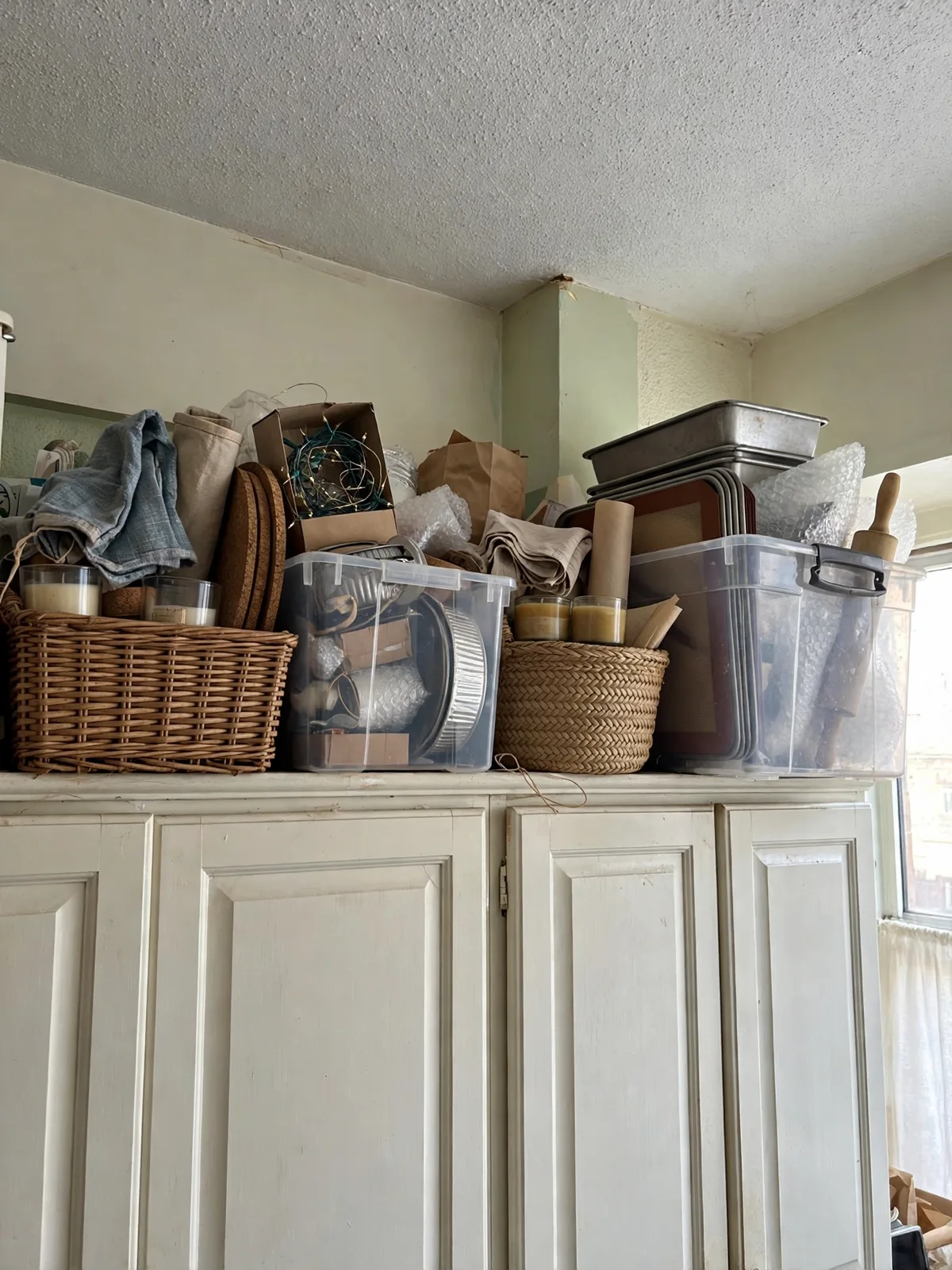Woven baskets and clear bins lined up on top of kitchen cabinets in a small apartment, storing rarely used items
