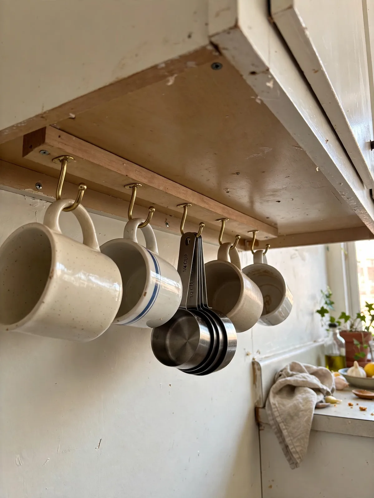 Row of hooks under a kitchen cabinet in a small apartment holding mugs and measuring cups hanging neatly above the counter