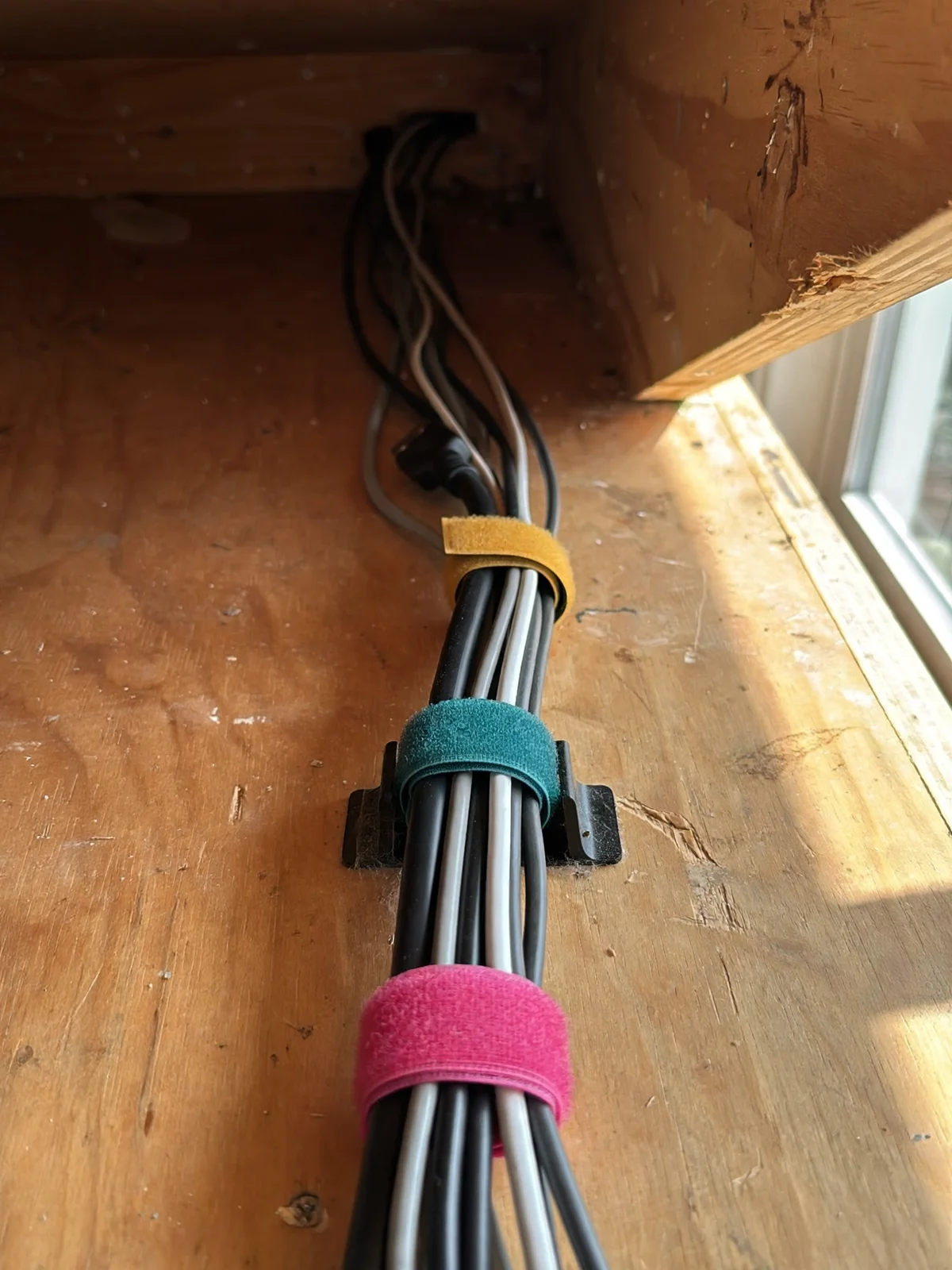 Bundle of black, white and grey desk cables held together in a neat parallel line with yellow, teal and pink Velcro cable ties
