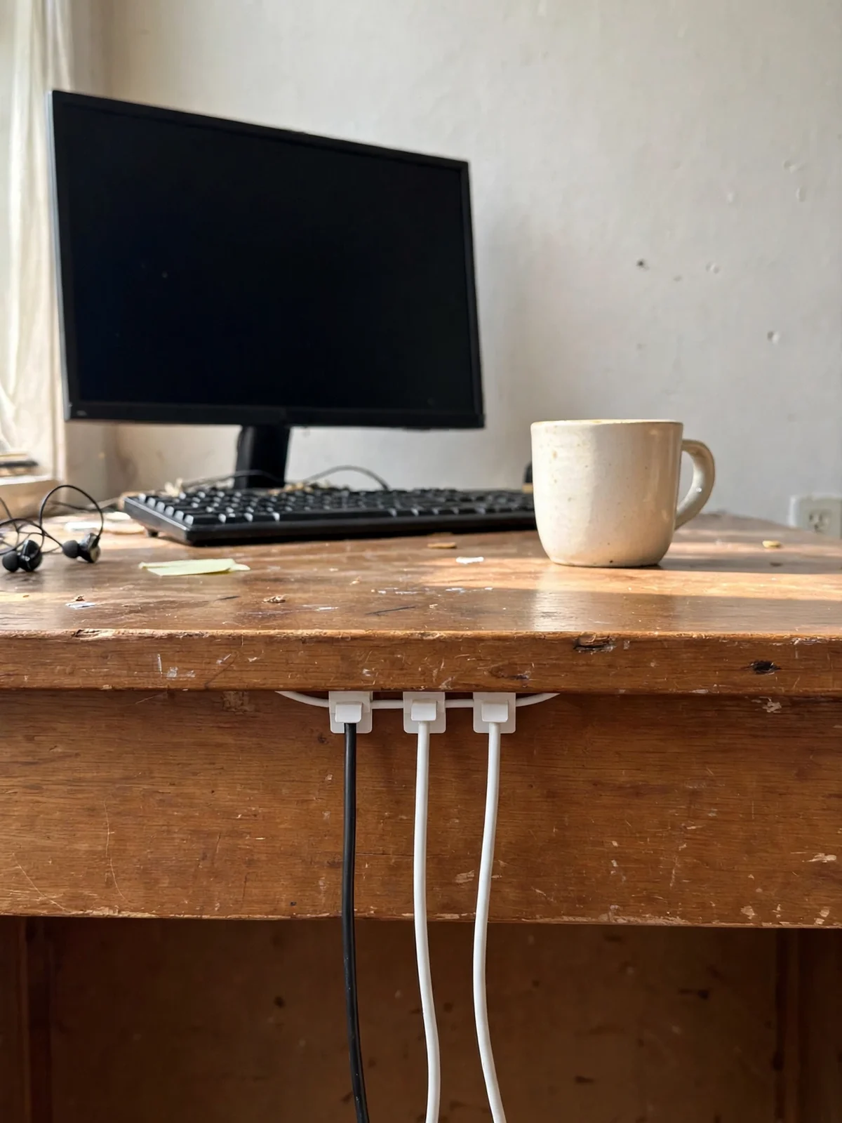 Three cables held by small white adhesive clips under the edge of a wooden desk, dropping straight down instead of sliding off the back
