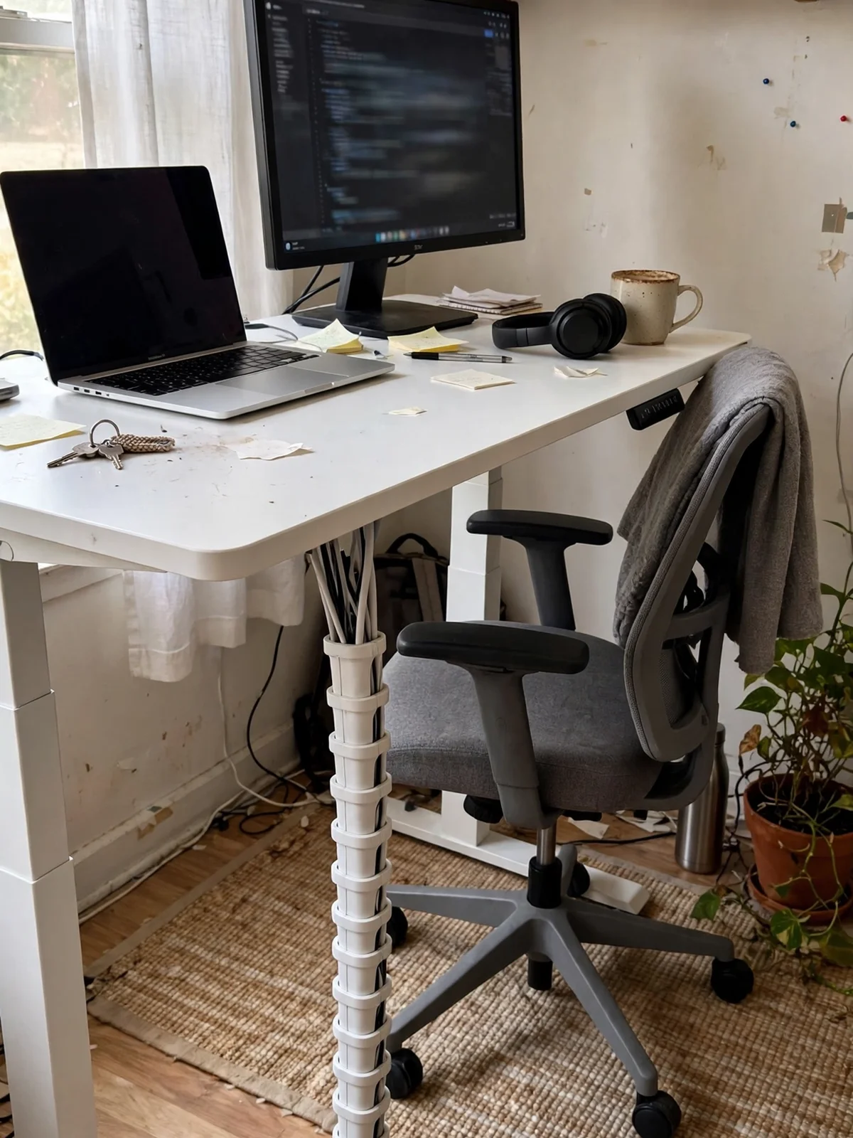 White segmented cable spine running from the underside of a raised standing desk down to the floor carrying all the desk cables in one column
