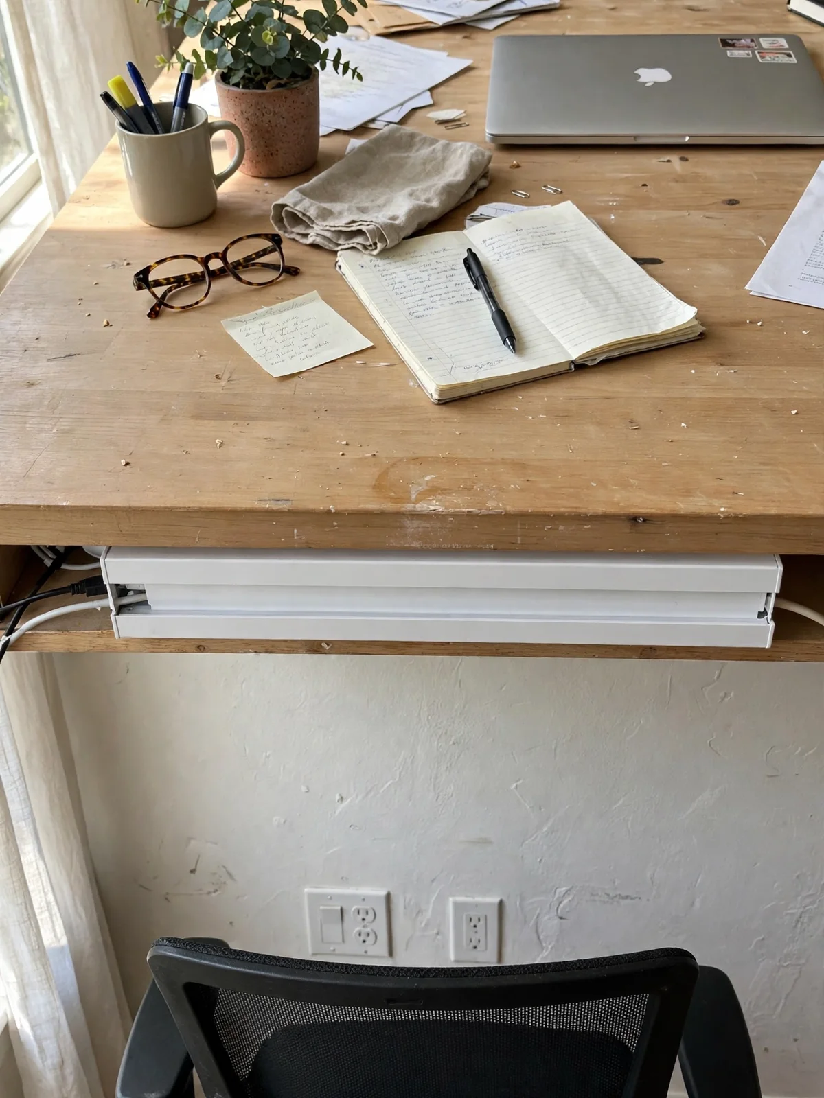 White cable raceway channel mounted under the back of a wooden desk with its cover on, cables entering one end and leaving the other hidden
