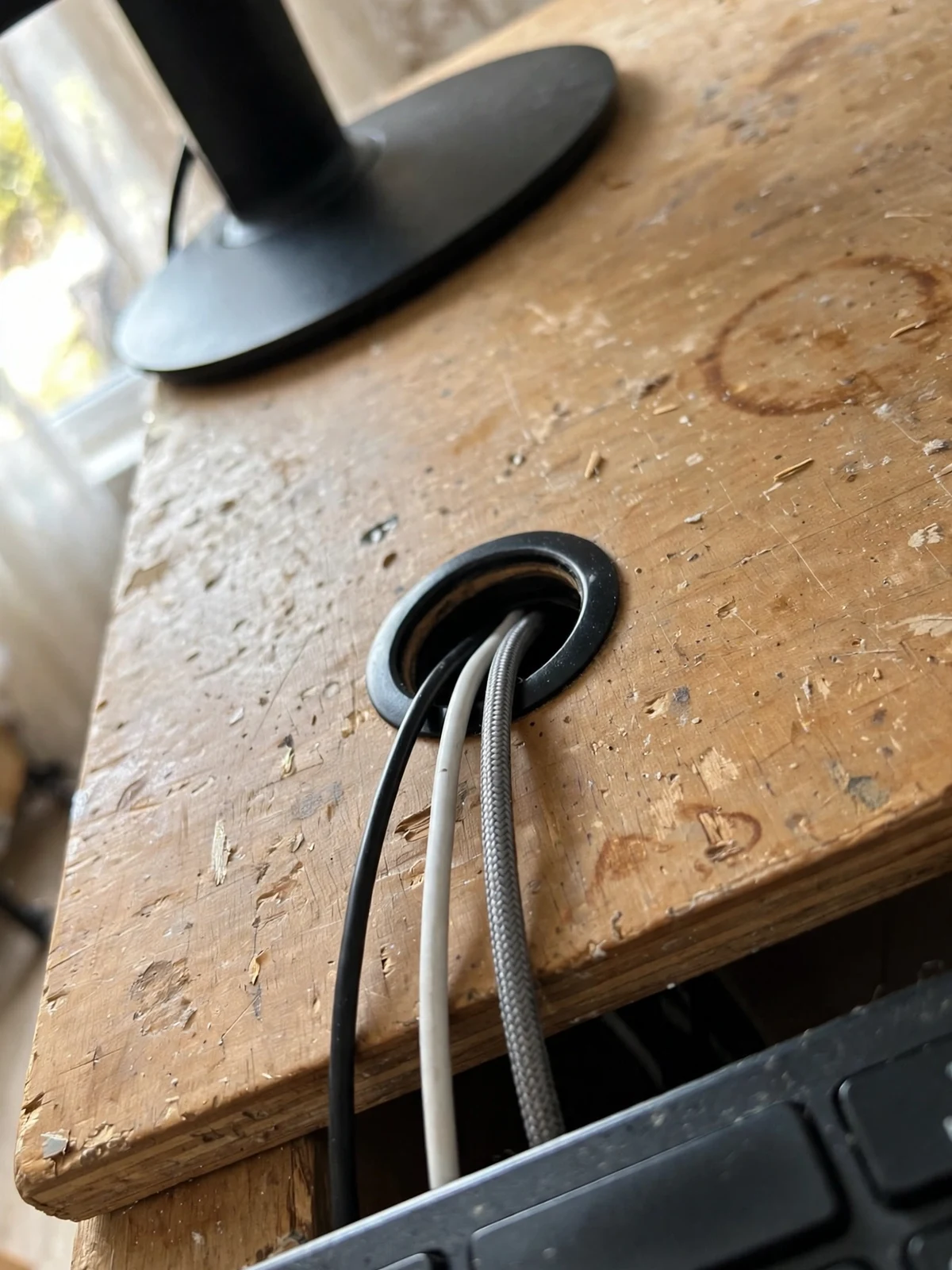 Top-down view of a wooden desktop with a black desk grommet in the corner and a black and a white cable passing down through it