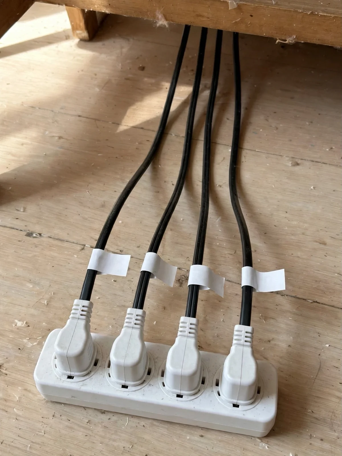 White power strip under a desk with four plugs in a neat row, each black cord marked with a small blank white cable label tag