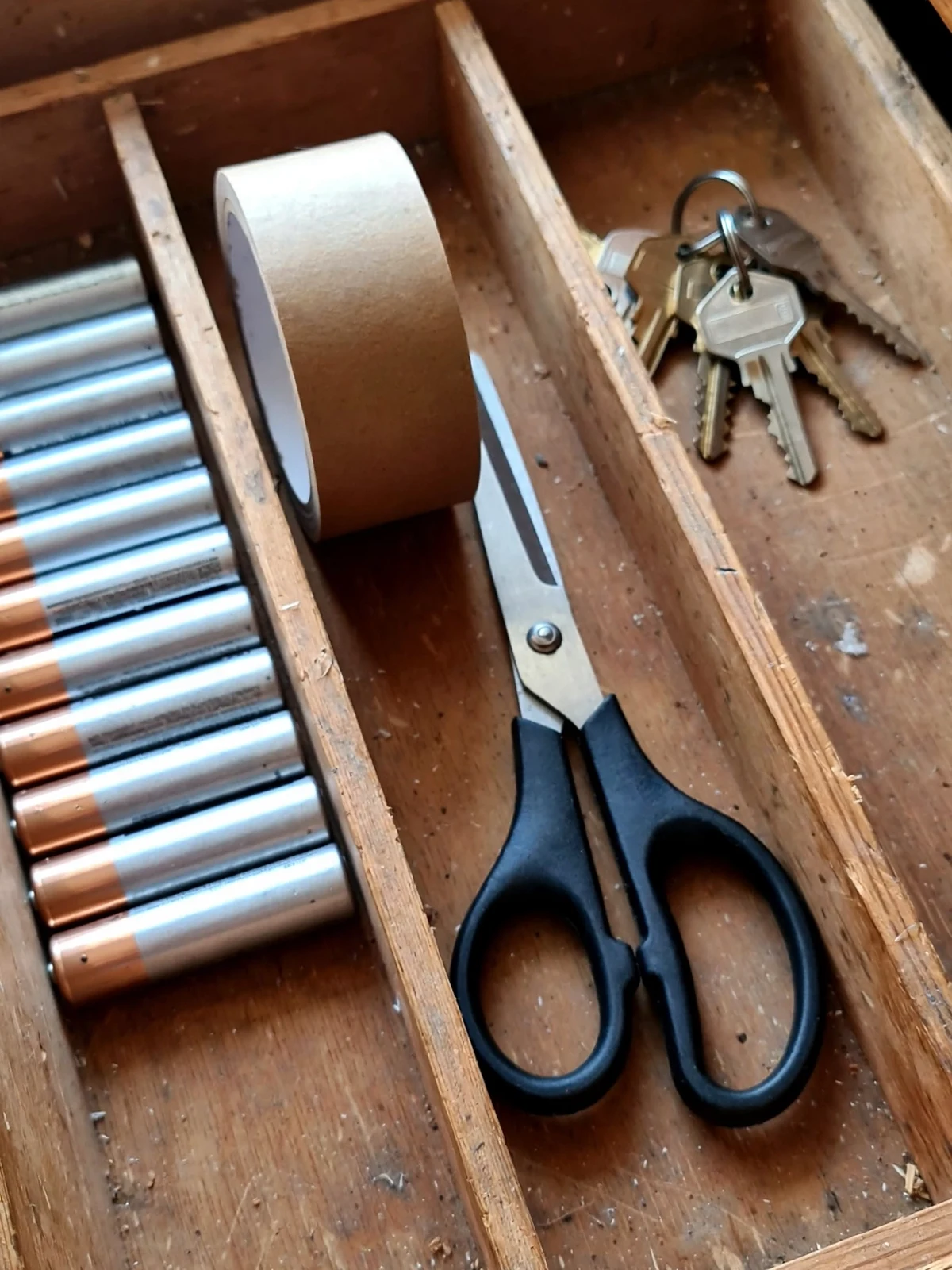 An organised junk drawer with dividers keeping batteries, tape, scissors and spare keys in their own sections