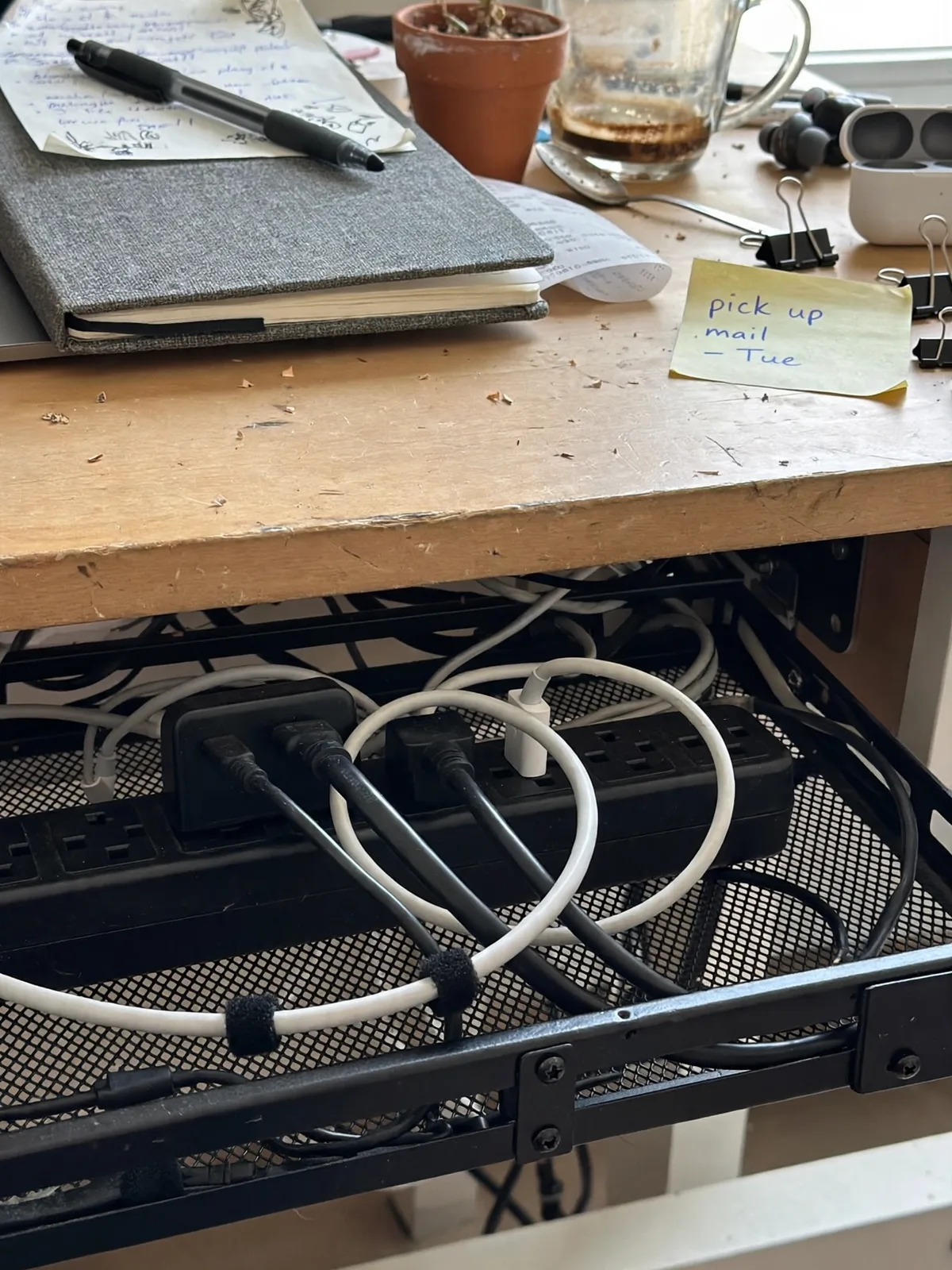 Back edge of a small desk showing a black cable management tray mounted underneath with a power strip and neatly routed cables hidden away