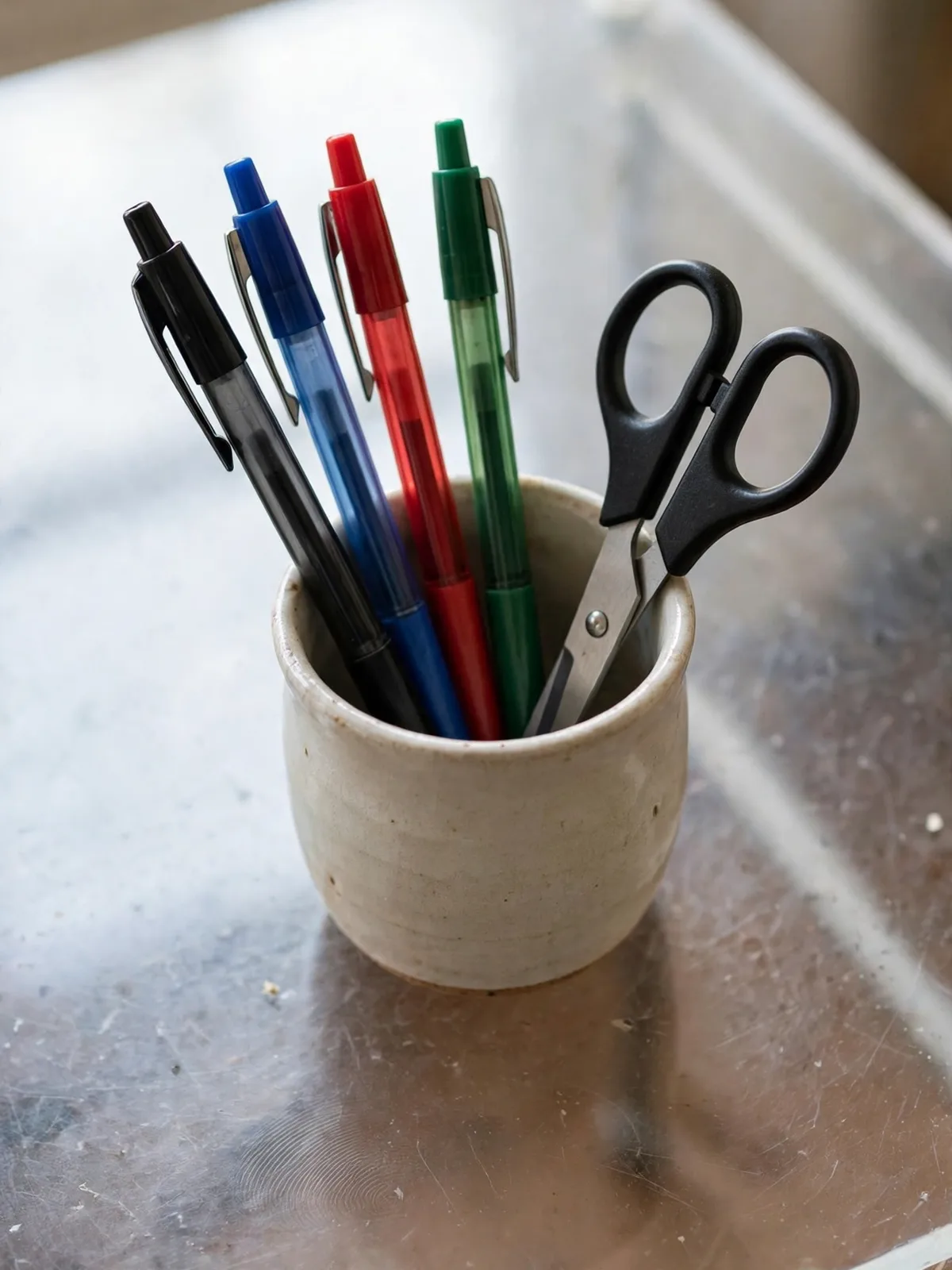 Small ceramic pen cup on a clear desk holding only four pens and a pair of scissors, minimal and ready for focused work