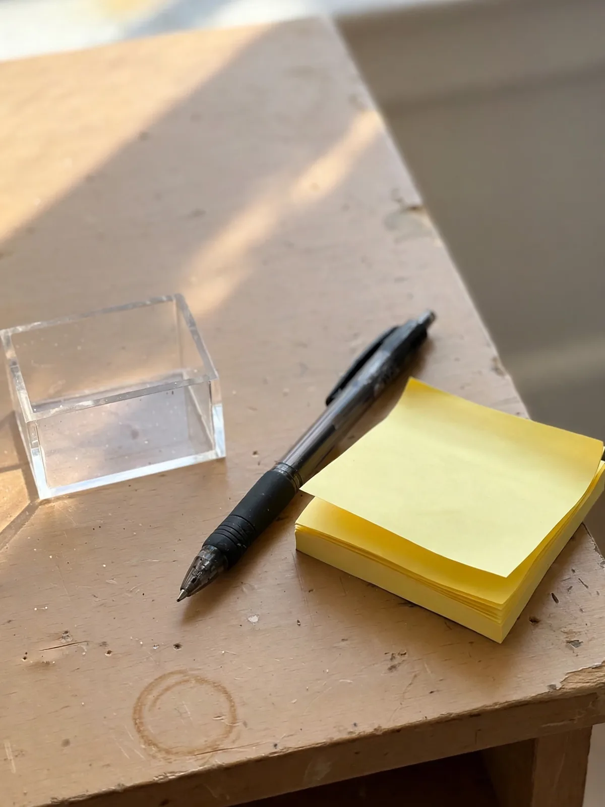 Single neat stack of sticky notes in an acrylic holder in one corner of a tidy small desk next to a pen
