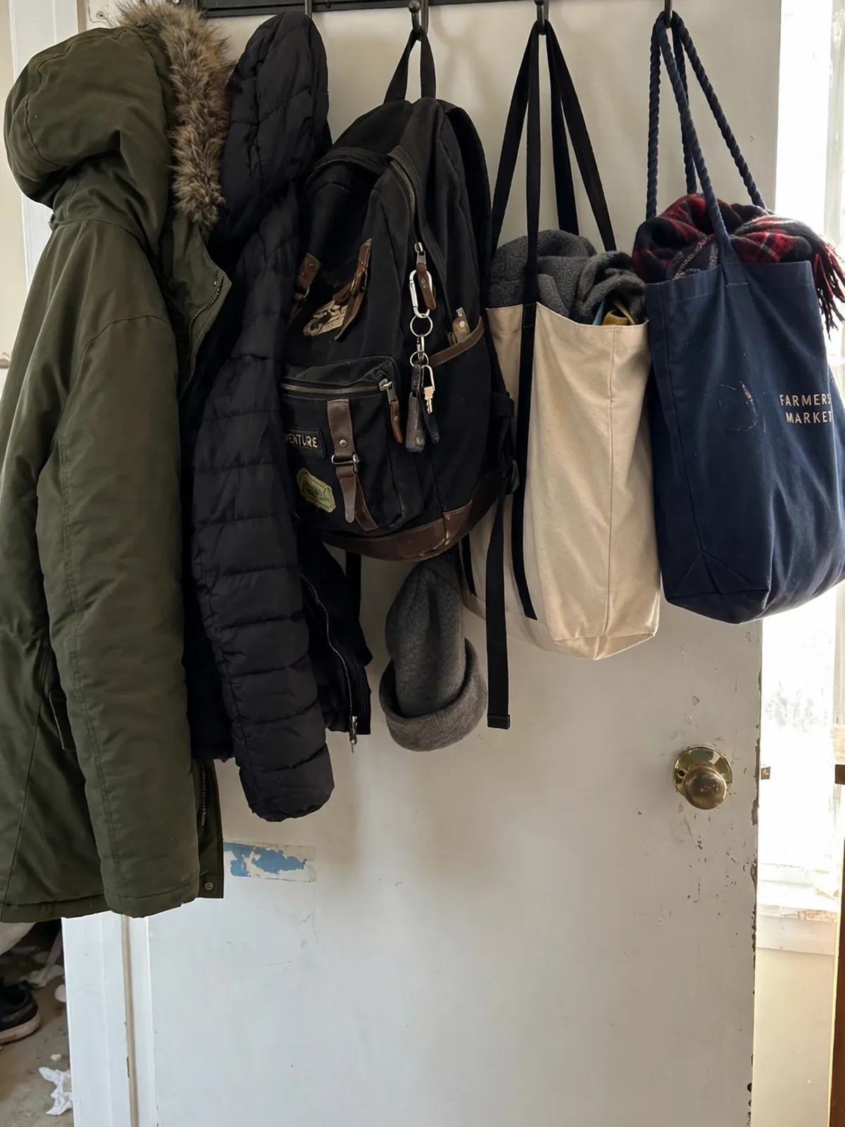 Heavy duty metal hook rail over a bedroom door holding winter coats a backpack and tote bags on strong wide hooks