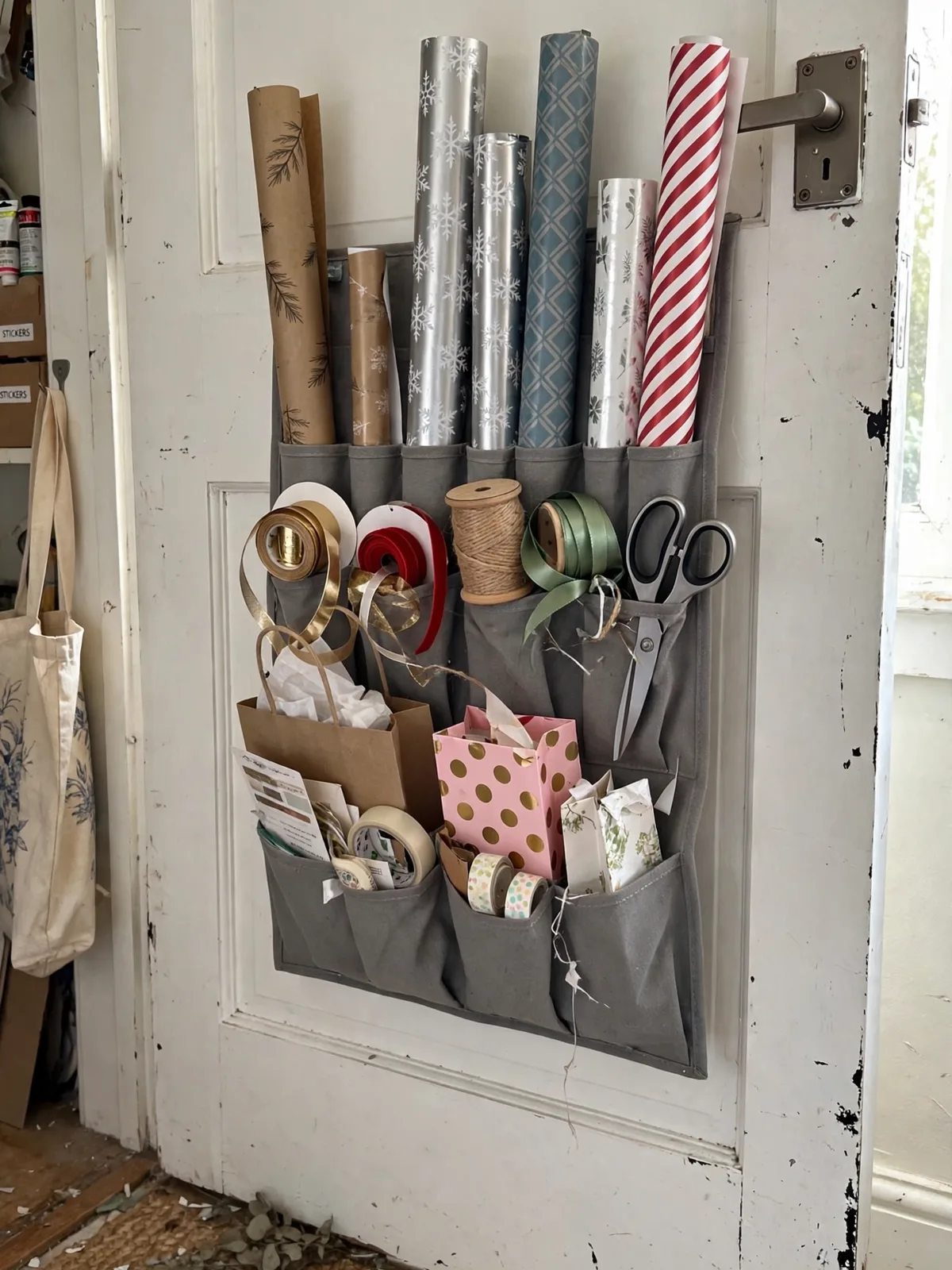 Gift wrap station hanging on a craft room door with rolls of wrapping paper ribbon spools scissors tape and gift bags organized vertically