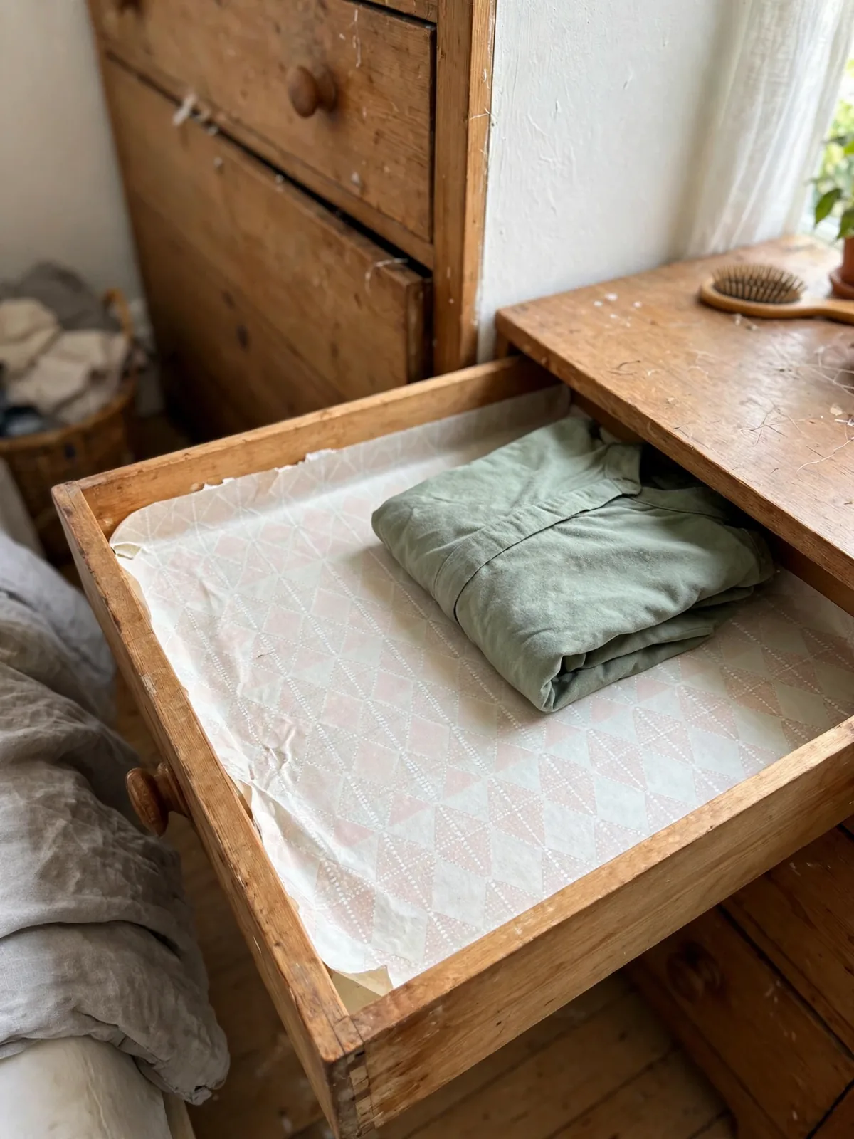 Open dresser drawer lined with light patterned non-slip liner and a folded shirt resting on top