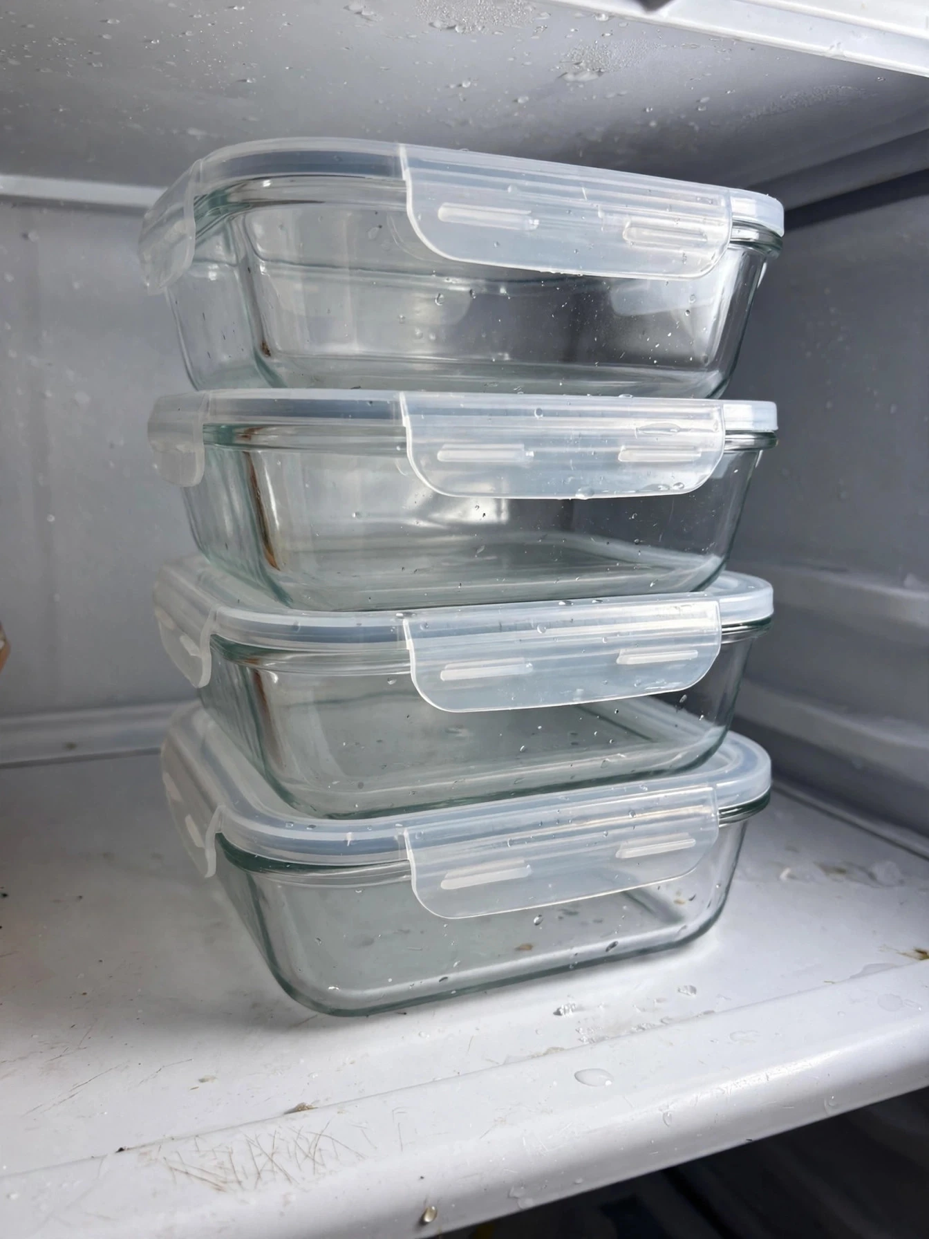 Matching clear glass leftover containers stacked neatly on a fridge shelf