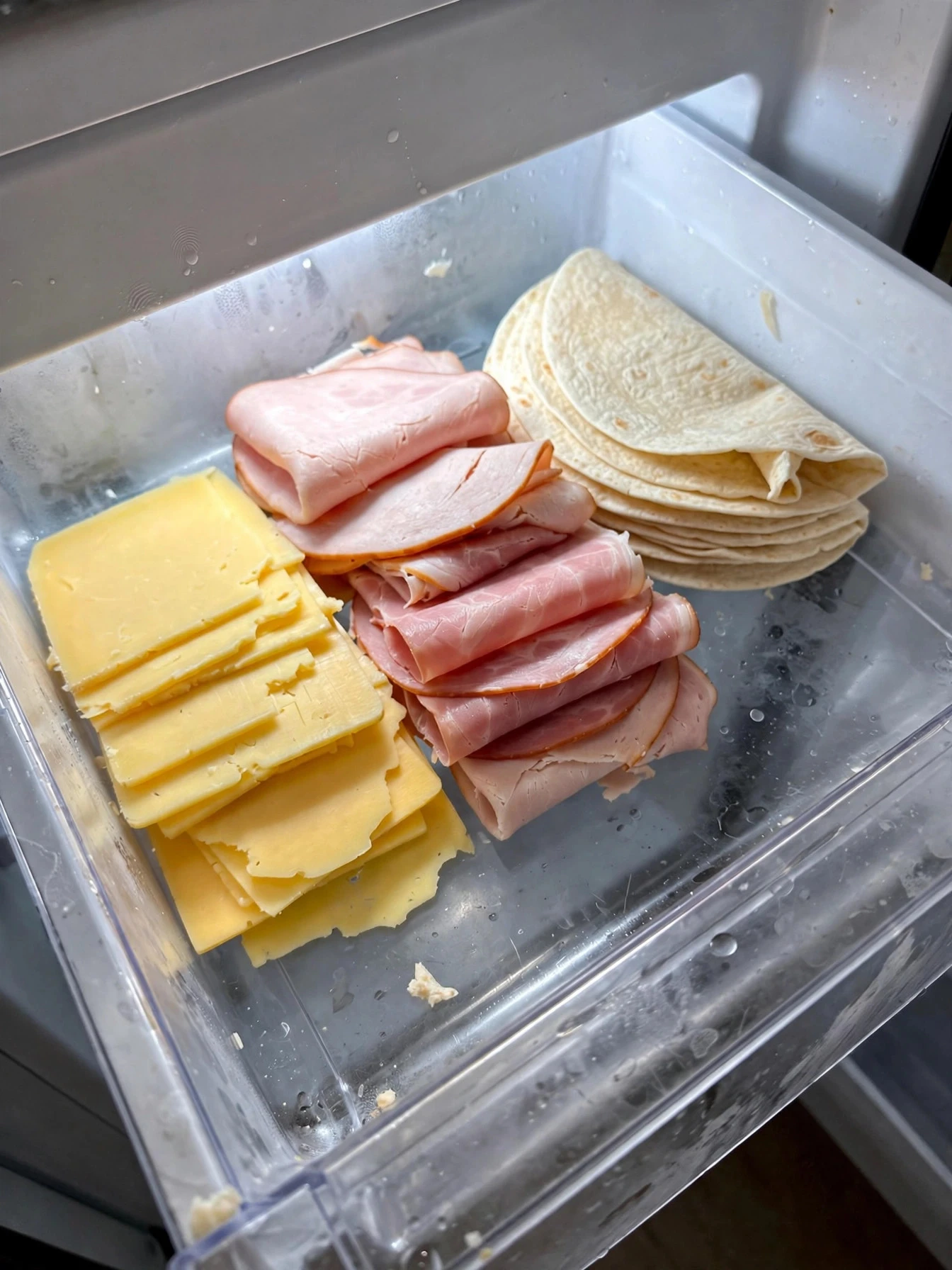 Deli drawer with sliced cheese, deli meats and tortillas arranged neatly