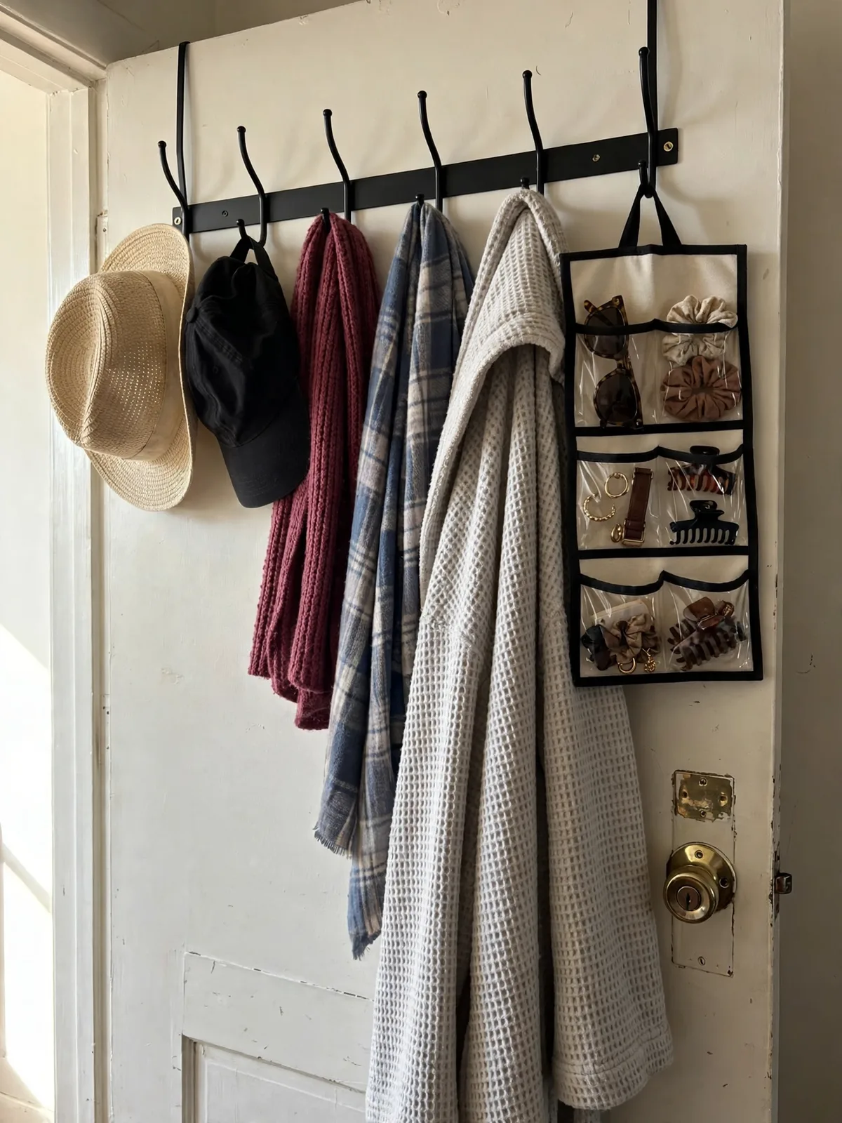 Back of a bedroom door with an over-door hook rack holding hats, scarves, a robe and accessories